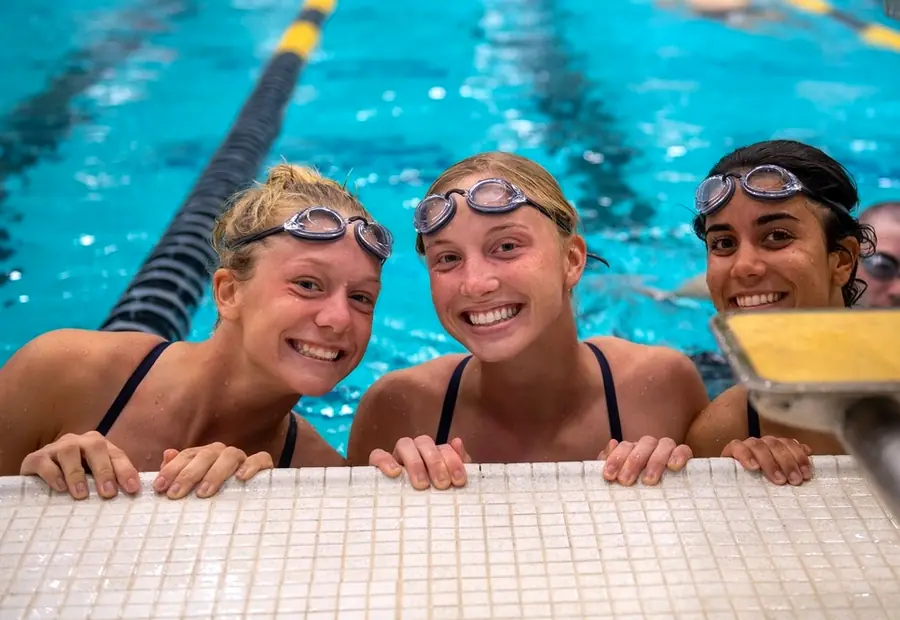 Three smiling swimmers in goggles at the pool wall